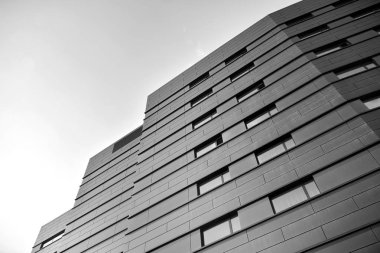 A view at a straight facade of a modern building with a dark grey facade. Dark grey metallic panel facad. Modern architectural details. Black and white.