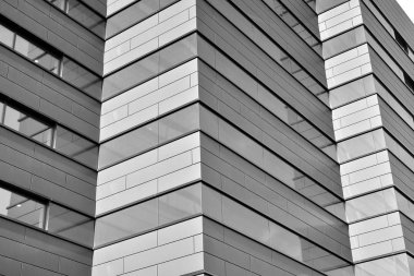 A view at a straight facade of a modern building with a dark grey facade. Dark grey metallic panel facad. Modern architectural details. Black and white.