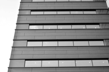 A view at a straight facade of a modern building with a dark grey facade. Dark grey metallic panel facad. Modern architectural details. Black and white.