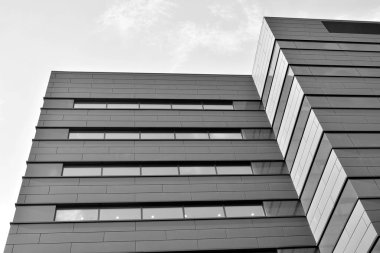 A view at a straight facade of a modern building with a dark grey facade. Dark grey metallic panel facad. Modern architectural details. Black and white.