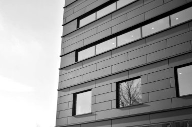 A view at a straight facade of a modern building with a dark grey facade. Dark grey metallic panel facad. Modern architectural details. Black and white.