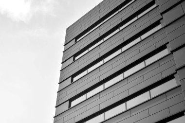 A view at a straight facade of a modern building with a dark grey facade. Dark grey metallic panel facad. Modern architectural details. Black and white.