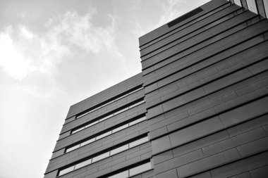 A view at a straight facade of a modern building with a dark grey facade. Dark grey metallic panel facad. Modern architectural details. Black and white.