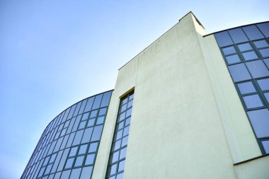 Modern bir ofis veya ticari binanın ön cephesinde cam şeffaf pencereler. Büyük bir şehrin merkezine inşa edilen bina mavi gökyüzünü yansıtır..