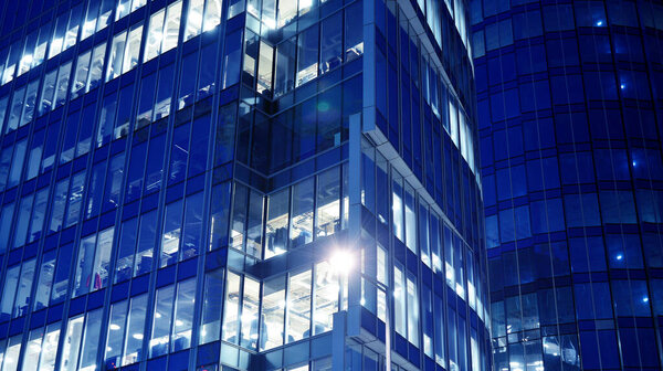 Night architecture - building with glass facade. Blue color of night lights. Modern building in business district. Concept of economics, financial.