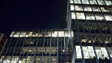 Ofis binalarının pencereleri gece aydınlandı. Şehir merkezinde yansıması olan cam mimari cephe tasarımı ile ışıklandırma.