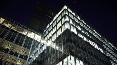Ofis binalarının pencereleri gece aydınlandı. Şehir merkezinde yansıması olan cam mimari cephe tasarımı ile ışıklandırma.