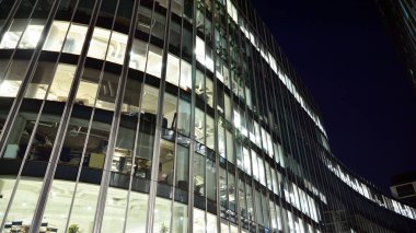 Ofis binalarının pencereleri gece aydınlandı. Şehir merkezinde yansıması olan cam mimari cephe tasarımı ile ışıklandırma.