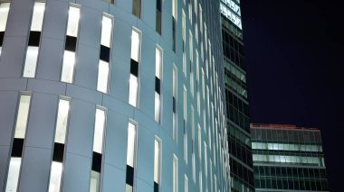 Ofis binalarının pencereleri gece aydınlandı. Şehir merkezinde yansıması olan cam mimari cephe tasarımı ile ışıklandırma.