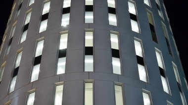 Ofis binalarının pencereleri gece aydınlandı. Şehir merkezinde yansıması olan cam mimari cephe tasarımı ile ışıklandırma.