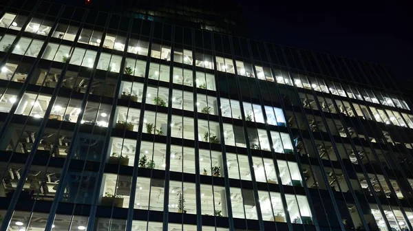 Pattern of office buildings windows illuminated at night. Lighting with Glass architecture facade design with reflection in urban city.