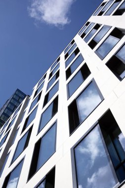 Camdan ve çelikten yapılmış modern perde duvarı. Mavi gökyüzü ve bulutlar modern ofis binasının camlarına yansıyor. 