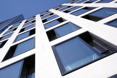 Camdan ve çelikten yapılmış modern perde duvarı. Mavi gökyüzü ve bulutlar modern ofis binasının camlarına yansıyor. 