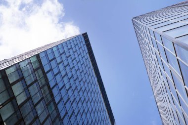 Camdan ve çelikten yapılmış modern perde duvarı. Mavi gökyüzü ve bulutlar modern ofis binasının camlarına yansıyor. 