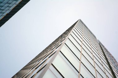 Camdan ve çelikten yapılmış modern perde duvarı. Mavi gökyüzü ve bulutlar modern ofis binasının camlarına yansıyor. 