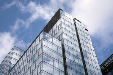 Camdan ve çelikten yapılmış modern perde duvarı. Mavi gökyüzü ve bulutlar modern ofis binasının camlarına yansıyor. 