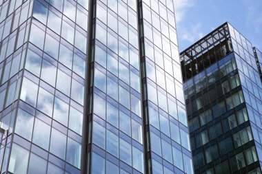 Camdan ve çelikten yapılmış modern perde duvarı. Mavi gökyüzü ve bulutlar modern ofis binasının camlarına yansıyor. 