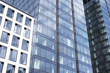 Camdan ve çelikten yapılmış modern perde duvarı. Mavi gökyüzü ve bulutlar modern ofis binasının camlarına yansıyor. 