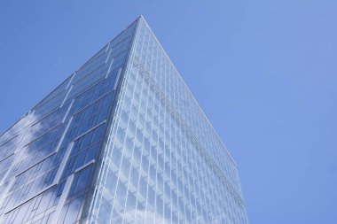 Camdan ve çelikten yapılmış modern perde duvarı. Mavi gökyüzü ve bulutlar modern ofis binasının camlarına yansıyor. 