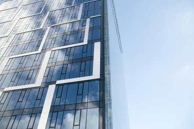 Camdan ve çelikten yapılmış modern perde duvarı. Mavi gökyüzü ve bulutlar modern ofis binasının camlarına yansıyor. 