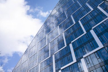 Camdan ve çelikten yapılmış modern perde duvarı. Mavi gökyüzü ve bulutlar modern ofis binasının camlarına yansıyor. 