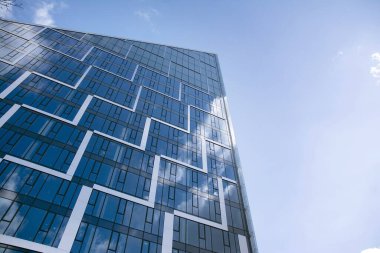 Camdan ve çelikten yapılmış modern perde duvarı. Mavi gökyüzü ve bulutlar modern ofis binasının camlarına yansıyor. 