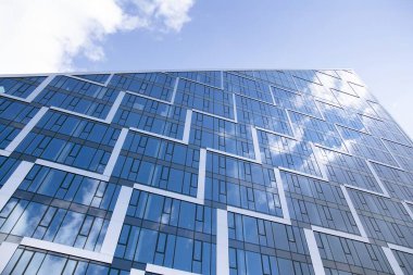 Camdan ve çelikten yapılmış modern perde duvarı. Mavi gökyüzü ve bulutlar modern ofis binasının camlarına yansıyor. 