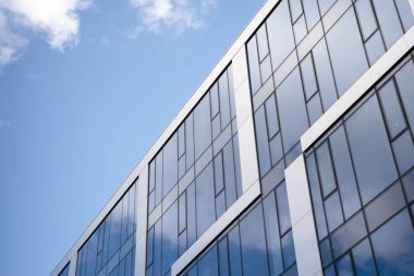 Camdan ve çelikten yapılmış modern perde duvarı. Mavi gökyüzü ve bulutlar modern ofis binasının camlarına yansıyor. 