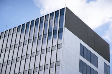 Camdan ve çelikten yapılmış modern perde duvarı. Mavi gökyüzü ve bulutlar modern ofis binasının camlarına yansıyor. 