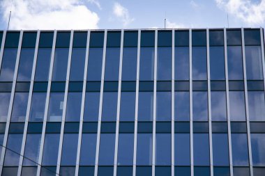 Camdan ve çelikten yapılmış modern perde duvarı. Mavi gökyüzü ve bulutlar modern ofis binasının camlarına yansıyor. 