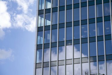 Camdan ve çelikten yapılmış modern perde duvarı. Mavi gökyüzü ve bulutlar modern ofis binasının camlarına yansıyor. 