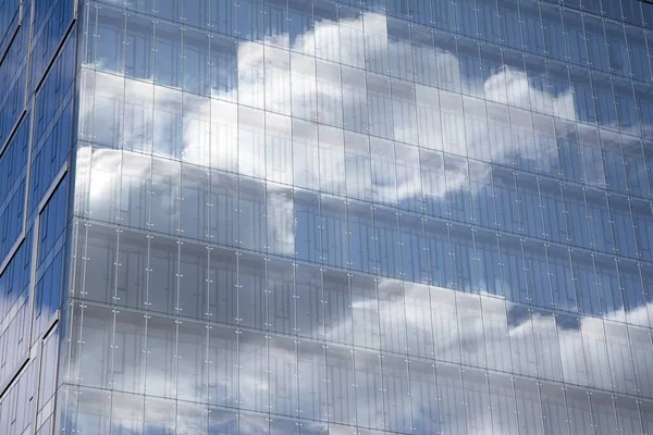 Modern curtain wall made of glass and steel. Blue sky and clouds reflected in windows of modern office building.