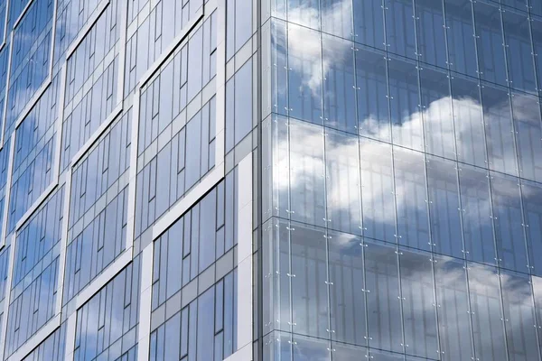 Modern curtain wall made of glass and steel. Blue sky and clouds reflected in windows of modern office building.