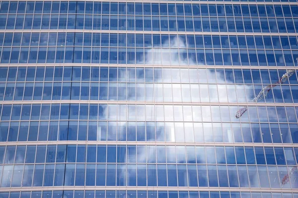 Modern curtain wall made of glass and steel. Blue sky and clouds reflected in windows of modern office building.