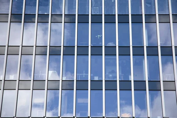 Modern curtain wall made of glass and steel. Blue sky and clouds reflected in windows of modern office building.