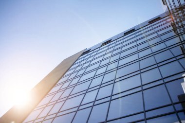 Günbatımında modern cam bina cephesi. Sıcak ve serin ton kontrastı. Güneş parlaması.