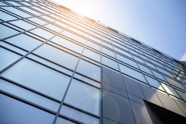 Günbatımında modern cam bina cephesi. Sıcak ve serin ton kontrastı. Güneş parlaması.