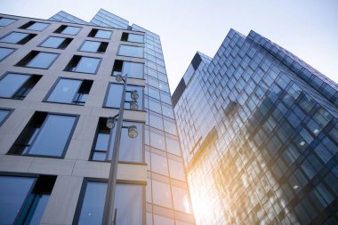 Gökdelen, şehirde günışığı olan modern bir bina. Gün ışığında bir ofis binasının cam duvarı. Ofis penceresi gün doğumu, yansıma ve perspektifle kapanıyor.