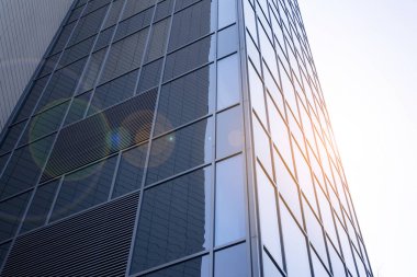 Gökdelen, şehirde günışığı olan modern bir bina. Gün ışığında bir ofis binasının cam duvarı. Ofis penceresi gün doğumu, yansıma ve perspektifle kapanıyor.