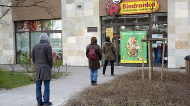 Varşova, Polonya. 3 Nisan 2020. Koronavirüs salgını sırasında kurallara uymak için marketin önünde sıra bekleyen insanlar.