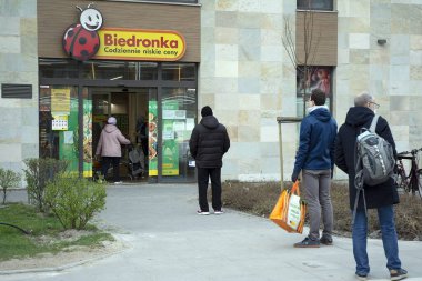 Varşova, Polonya. 3 Nisan 2020. Koronavirüs salgını sırasında kurallara uymak için marketin önünde sıra bekleyen insanlar.