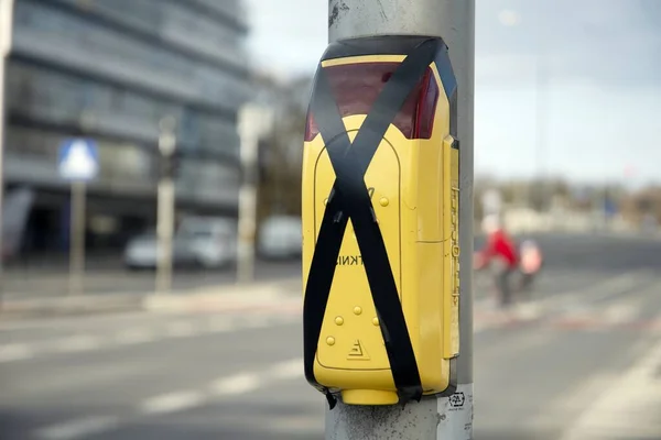 Yellow pedestrian crossing sign or pedestrian crossing button located on a metal pillar next to a pedestrian crossing on the street with black tape to avoid touching due to a coronavirus pandemic.