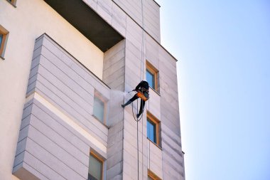 İp girişi bakım onarımı. Apartmanın dış cephesini temizleyen bir işçi..