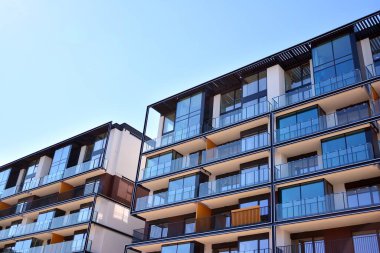 Mavi gökyüzü olan güneşli bir günde modern ve yeni bir apartman. Gündüz gözüyle çağdaş yerleşim yerinin dış tarafında..