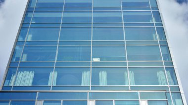Dikey çizgileri ve yansıması olan modern ofis pencereleri. Gökyüzünü bulutlarla yansıtıyor ve gerçeküstü bir manzara yaratıyor..