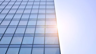 Ofis binasının alt manzarası gün doğumu, yansıma ve perspektifle kapanıyor. Güneş ışınlı modern mimari. Parlak güneşli bir günde, masmavi gökyüzünde güneş ışınlarıyla cam cephe. 