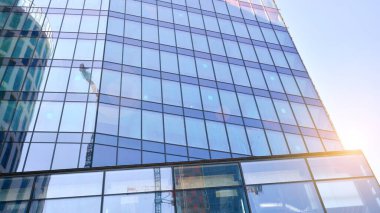 Ofis binasının alt manzarası gün doğumu, yansıma ve perspektifle kapanıyor. Güneş ışınlı modern mimari. Parlak güneşli bir günde, masmavi gökyüzünde güneş ışınlarıyla cam cephe. 