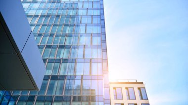 Ofis binasının alt manzarası gün doğumu, yansıma ve perspektifle kapanıyor. Güneş ışınlı modern mimari. Parlak güneşli bir günde, masmavi gökyüzünde güneş ışınlarıyla cam cephe. 