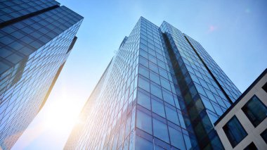 Ofis binasının alt manzarası gün doğumu, yansıma ve perspektifle kapanıyor. Güneş ışınlı modern mimari. Parlak güneşli bir günde, masmavi gökyüzünde güneş ışınlarıyla cam cephe. 