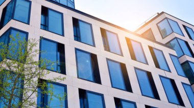 Ofis binasının alt manzarası gün doğumu, yansıma ve perspektifle kapanıyor. Güneş ışınlı modern mimari. Parlak güneşli bir günde, masmavi gökyüzünde güneş ışınlarıyla cam cephe. 